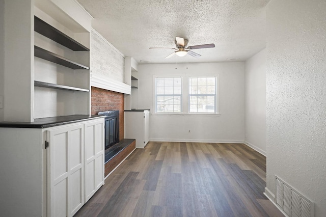 unfurnished living room featuring built in shelves, a textured ceiling, dark hardwood / wood-style flooring, ceiling fan, and a fireplace