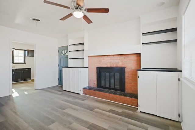 unfurnished living room featuring hardwood / wood-style floors, built in features, a brick fireplace, and ceiling fan