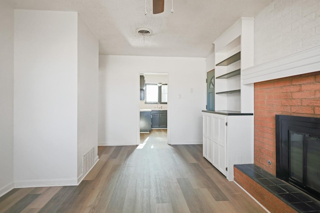 unfurnished living room with dark hardwood / wood-style floors, built in features, a fireplace, ceiling fan, and a textured ceiling