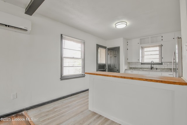 2014 60th St, Lubbock, TX 79412 - kitchen featuring a wall mounted AC, white cabinets, light wood-style floors, backsplash, and butcher block counters