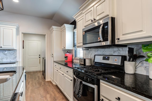 kitchen featuring white cabinetry, vaulted ceiling, dark stone countertops, and appliances with stainless steel finishes