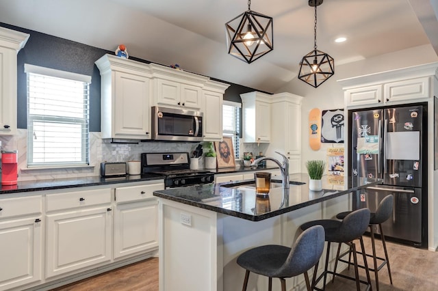 kitchen with sink, appliances with stainless steel finishes, pendant lighting, a kitchen island with sink, and white cabinets