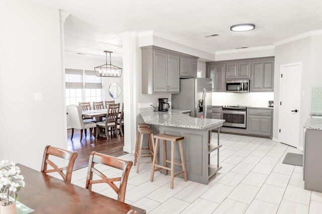 kitchen featuring a kitchen breakfast bar, tasteful backsplash, gray cabinetry, a peninsula, and appliances with stainless steel finishes