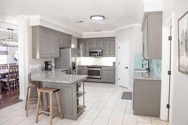 kitchen featuring ornamental molding, gray cabinetry, a sink, a peninsula, and appliances with stainless steel finishes