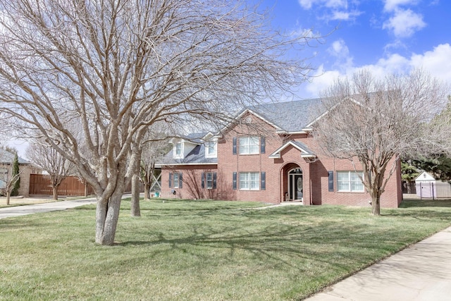 traditional-style home featuring brick siding, a front yard, and fence