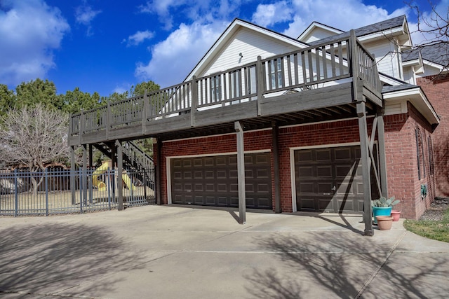 view of side of property with fence, a wooden deck, an attached garage, brick siding, and driveway