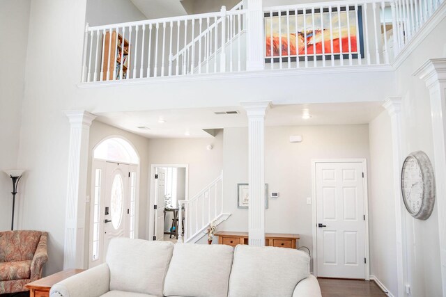 living room featuring decorative columns, visible vents, a towering ceiling, and stairway