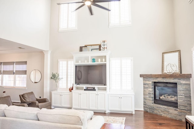 living area with a ceiling fan, a high ceiling, wood finished floors, a glass covered fireplace, and baseboards