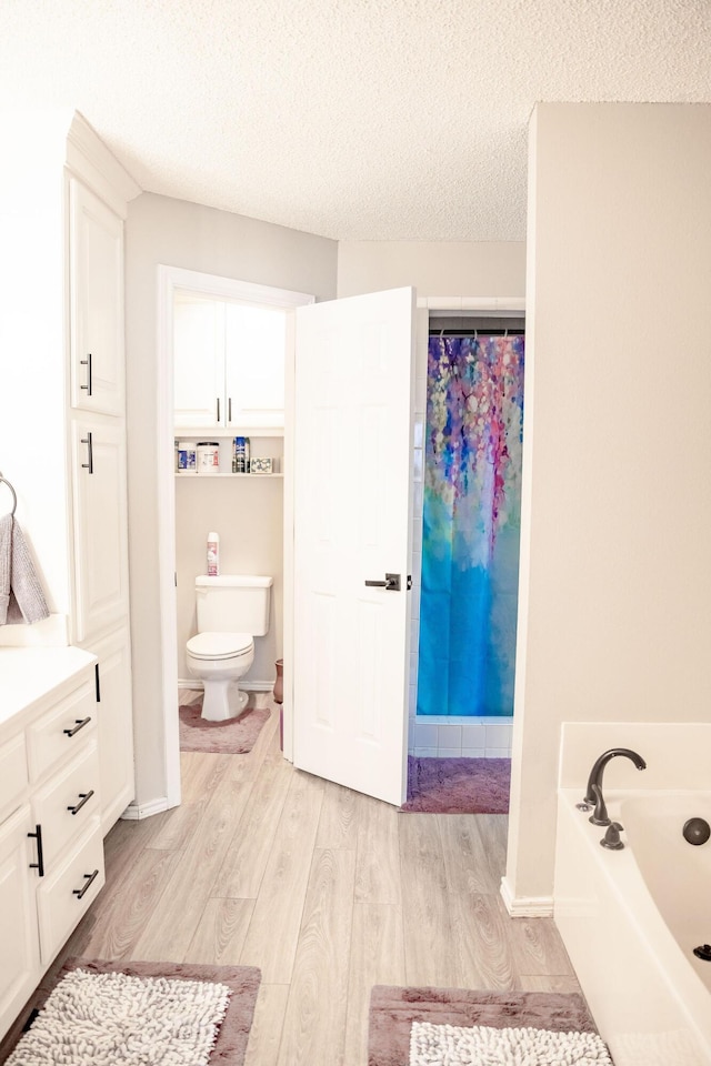 full bathroom featuring toilet, wood finished floors, a garden tub, and a textured ceiling