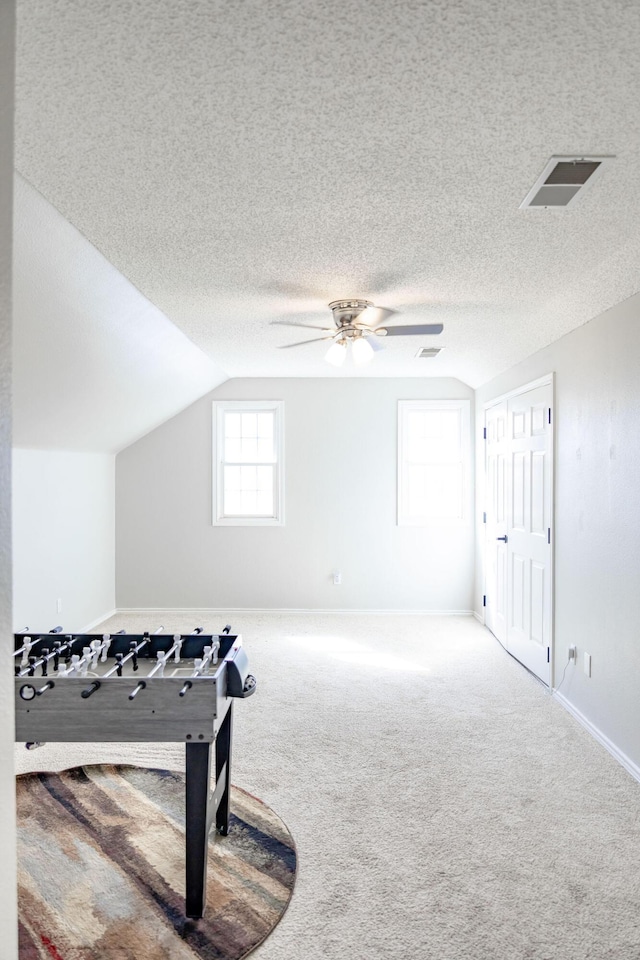 rec room with a textured ceiling, visible vents, carpet, ceiling fan, and lofted ceiling