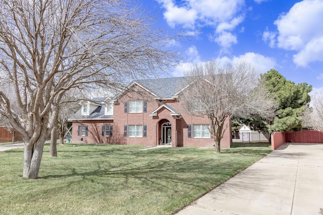 view of front facade featuring a shingled roof, a front yard, fence, and brick siding