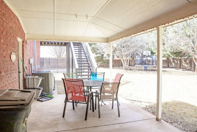 view of patio / terrace featuring central AC unit, a trampoline, outdoor dining space, stairway, and a fenced backyard