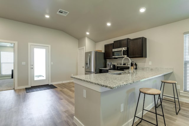 kitchen with a breakfast bar, sink, light stone counters, dark brown cabinets, and appliances with stainless steel finishes