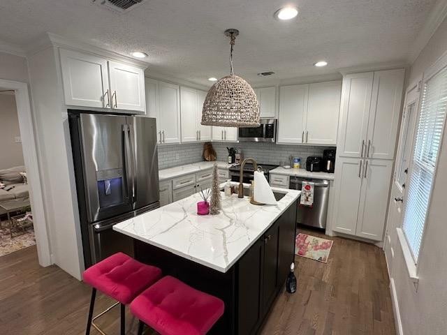 kitchen with pendant lighting, stainless steel appliances, a kitchen island with sink, and white cabinets