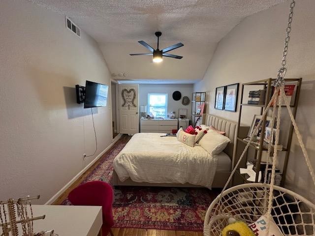 bedroom with ceiling fan, wood-type flooring, vaulted ceiling, and a textured ceiling