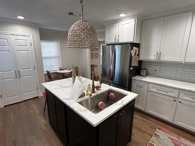 kitchen with hanging light fixtures, a center island with sink, white cabinets, and stainless steel refrigerator with ice dispenser