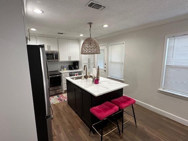 kitchen featuring sink, white cabinetry, hanging light fixtures, stainless steel appliances, and a center island with sink