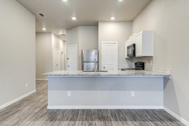 kitchen featuring kitchen peninsula, light stone counters, white cabinets, and black appliances