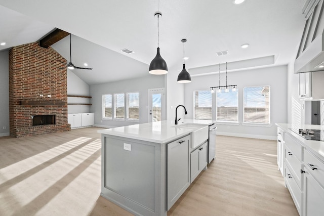 kitchen featuring sink, an island with sink, pendant lighting, a fireplace, and light hardwood / wood-style floors