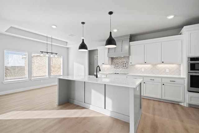 kitchen with pendant lighting, stainless steel double oven, a tray ceiling, a center island with sink, and black electric cooktop