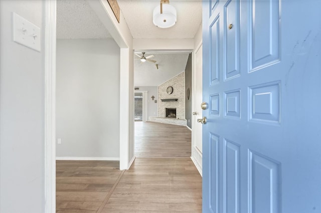 entrance foyer featuring ceiling fan, vaulted ceiling, a textured ceiling, and light wood-type flooring