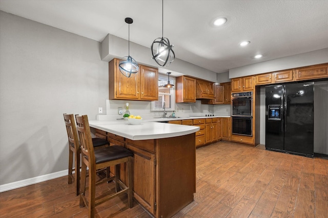 3808 27th St, Lubbock, TX 79410 - kitchen with black appliances, brown cabinetry, wood finished floors, a peninsula, and light countertops