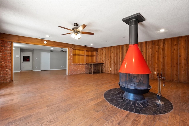 3808 27th St, Lubbock, TX 79410 - detailed view of a wood stove, ceiling fan, wood walls, wood finished floors, and a textured ceiling