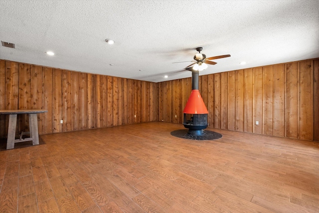 3808 27th St, Lubbock, TX 79410 - unfurnished living room with a wood stove, wood finished floors, a ceiling fan, a textured ceiling, and wood walls