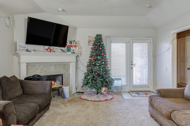 carpeted living room with a tiled fireplace, vaulted ceiling, and a textured ceiling