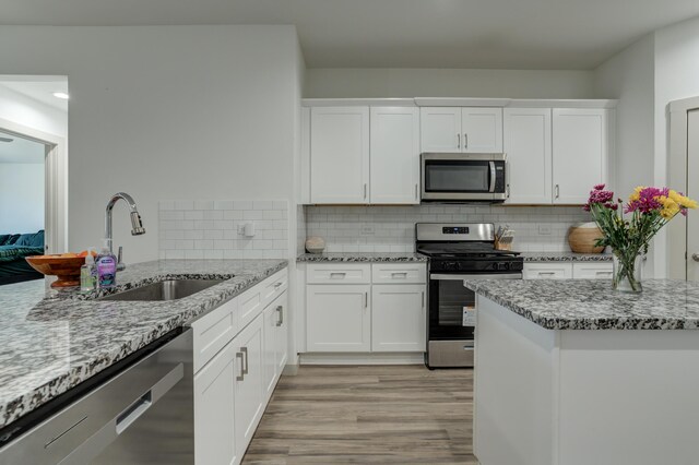 6904 56th St, Lubbock, TX 79407 - kitchen featuring appliances with stainless steel finishes, a sink, light wood-type flooring, white cabinets, and light stone counters