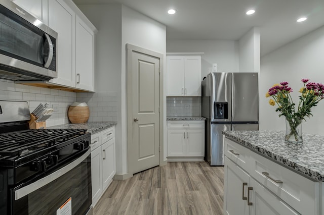 6904 56th St, Lubbock, TX 79407 - kitchen featuring appliances with stainless steel finishes, light wood finished floors, white cabinetry, decorative backsplash, and light stone counters