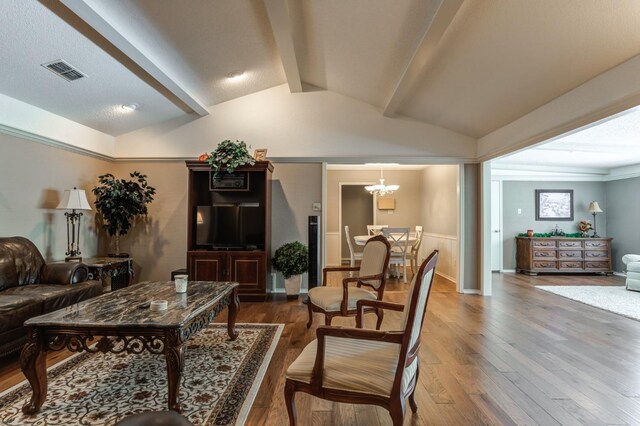 living room featuring lofted ceiling with beams, a chandelier, hardwood / wood-style floors, and a textured ceiling