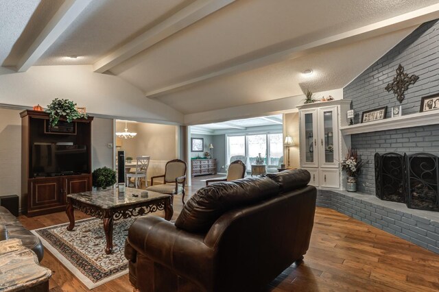 living room featuring a brick fireplace, vaulted ceiling with beams, hardwood / wood-style floors, and a chandelier