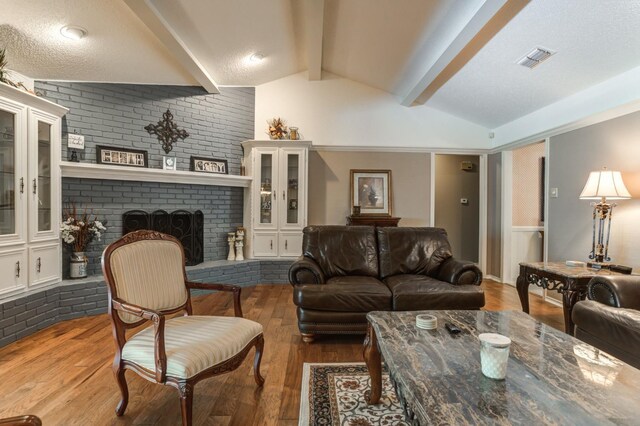 living room featuring lofted ceiling with beams, hardwood / wood-style floors, a textured ceiling, and a fireplace