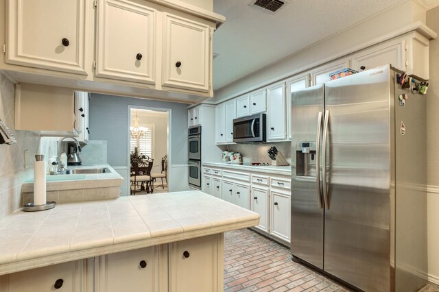 kitchen featuring appliances with stainless steel finishes, tile countertops, tasteful backsplash, sink, and a notable chandelier