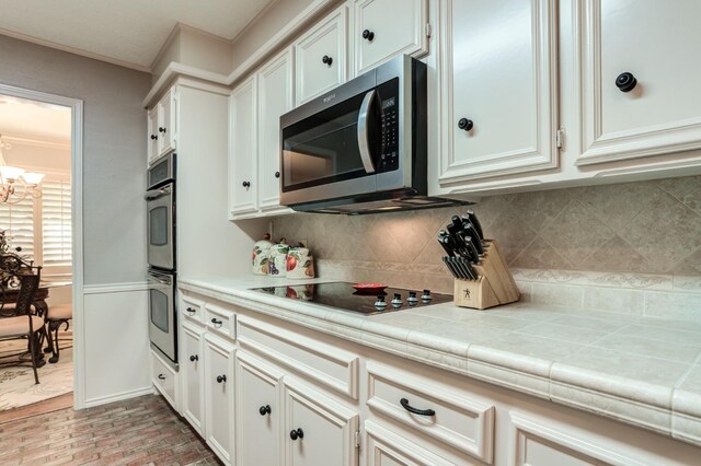 kitchen with tile countertops, white cabinets, decorative backsplash, ornamental molding, and stainless steel appliances