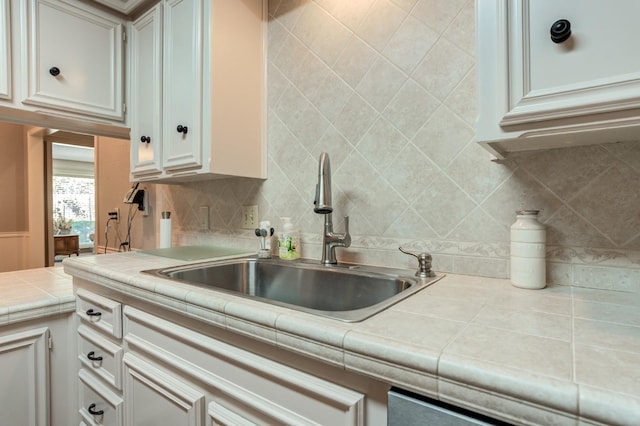 kitchen with tasteful backsplash, white cabinetry, sink, and tile counters