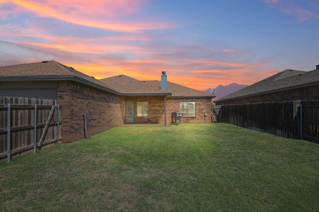 back house at dusk featuring a lawn