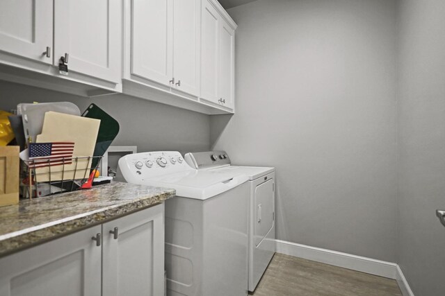 laundry area featuring cabinets, hardwood / wood-style flooring, and washing machine and clothes dryer