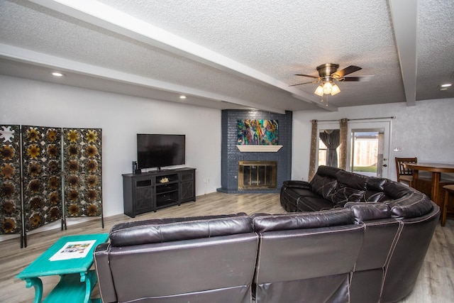 living room featuring ceiling fan, light wood-type flooring, a brick fireplace, and a textured ceiling