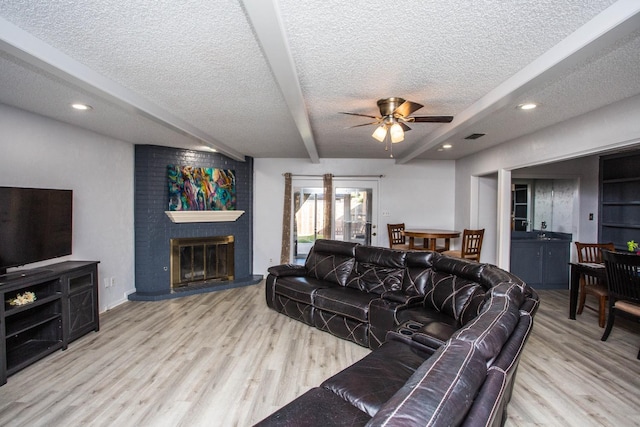 living room with a brick fireplace, beam ceiling, light hardwood / wood-style floors, and a textured ceiling