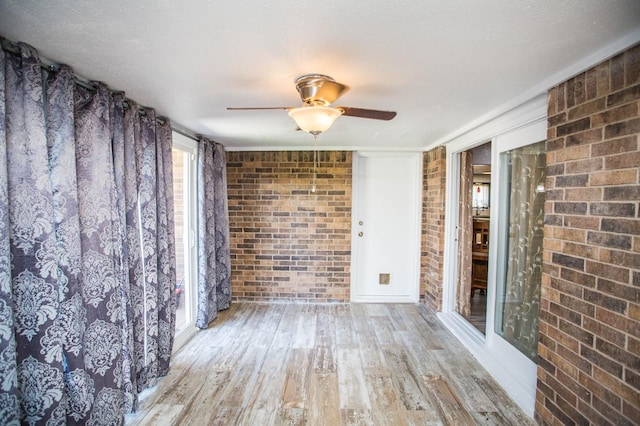 unfurnished room with brick wall, a textured ceiling, ceiling fan, and light hardwood / wood-style flooring