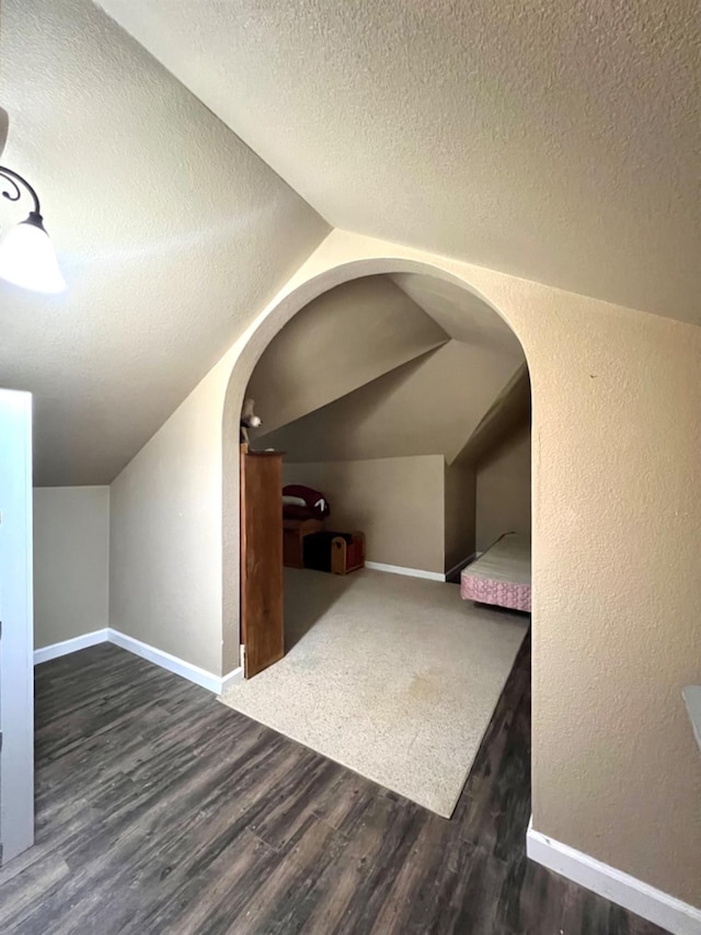 additional living space featuring lofted ceiling, dark hardwood / wood-style floors, and a textured ceiling