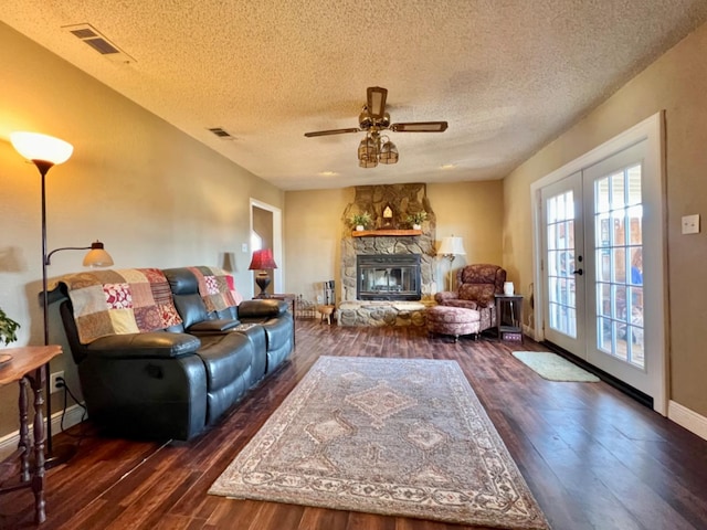 living room with a stone fireplace, dark wood-type flooring, ceiling fan, and french doors