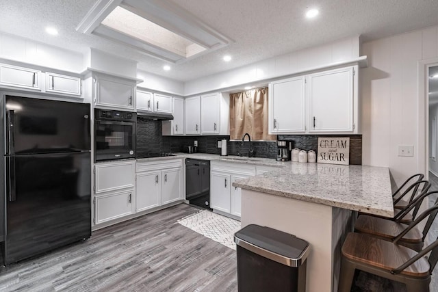 kitchen featuring black appliances, sink, white cabinets, light stone counters, and kitchen peninsula