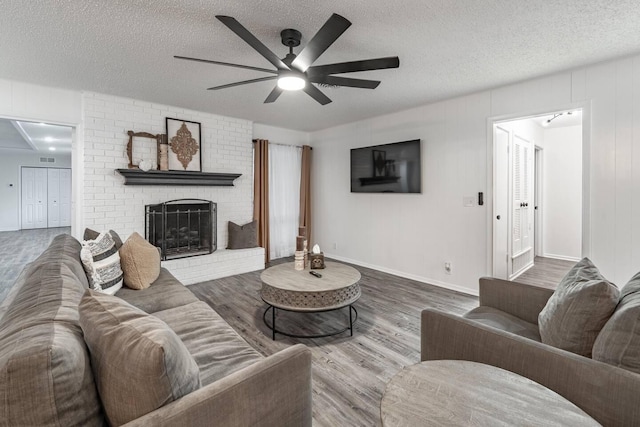 living room with a brick fireplace, hardwood / wood-style flooring, a textured ceiling, and ceiling fan