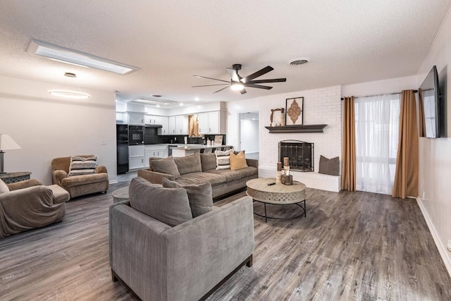 living room featuring a fireplace, wood-type flooring, a textured ceiling, and ceiling fan