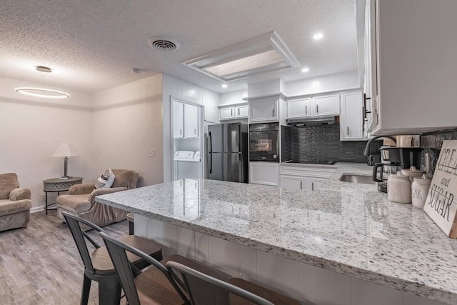 kitchen featuring washer / dryer, a breakfast bar area, black appliances, kitchen peninsula, and white cabinets