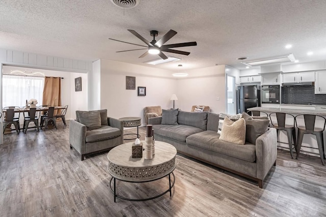 living room featuring ceiling fan, light hardwood / wood-style flooring, and a textured ceiling