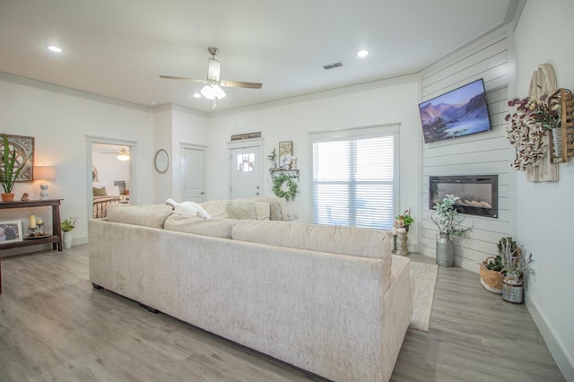 living room featuring crown molding, light hardwood / wood-style flooring, a large fireplace, and ceiling fan